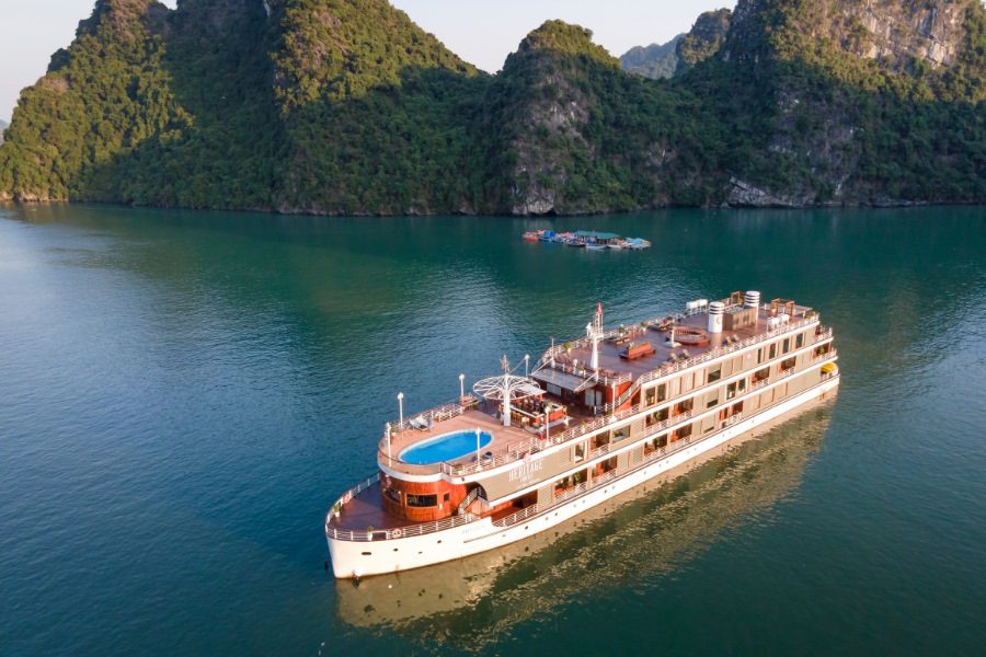 Luxury cruise ship with a pool on deck sailing through a scenic bay surrounded by lush green mountains and calm waters, perfect for a 8 days in Vietnam travel experience.