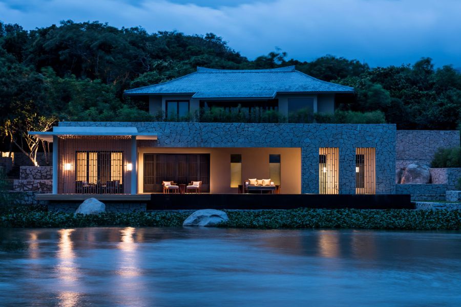 Serene beach resort villa in Vietnam at dusk, featuring a modern design with warm lighting, surrounded by water and lush greenery.