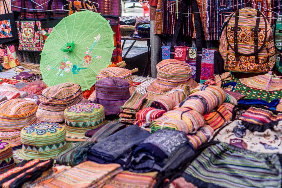 Colorful market stall displaying a variety of handwoven textiles, including hats, bags, and fabrics in vibrant patterns.