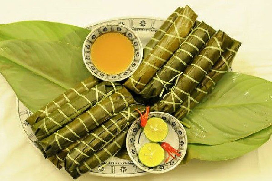 This image features banh gio, a traditional steamed rice cake wrapped in banana leaves, known for its soft, savory filling and often enjoyed with dipping sauce and fresh lime