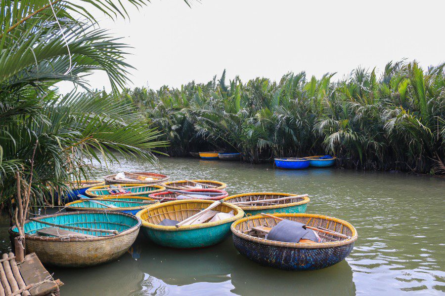 Cluster of colorful traditional Vietnamese basket boats on a calm river, surrounded by dense palm trees and lush greenery, offering a serene setting for cultural exploration and water activities.