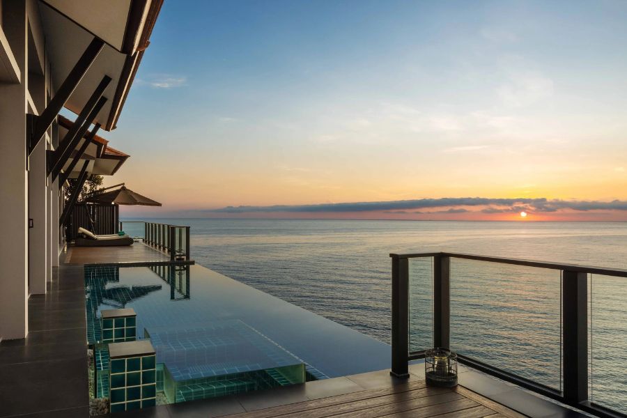 Stunning infinity pool at a Bayan Tree beach resort in Vietnam, overlooking the ocean with a breathtaking sunset view, featuring a spacious deck and lounge area.