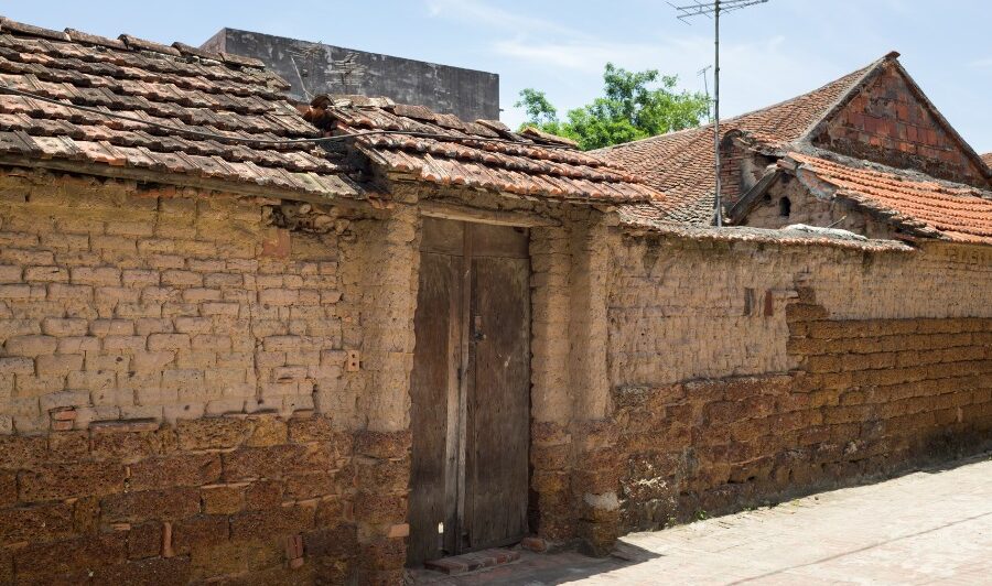 A weathered brick building with a tiled roof and a wooden door in Duong Lam village. The walls show signs of age and wear, with a mix of brick and mud construction.