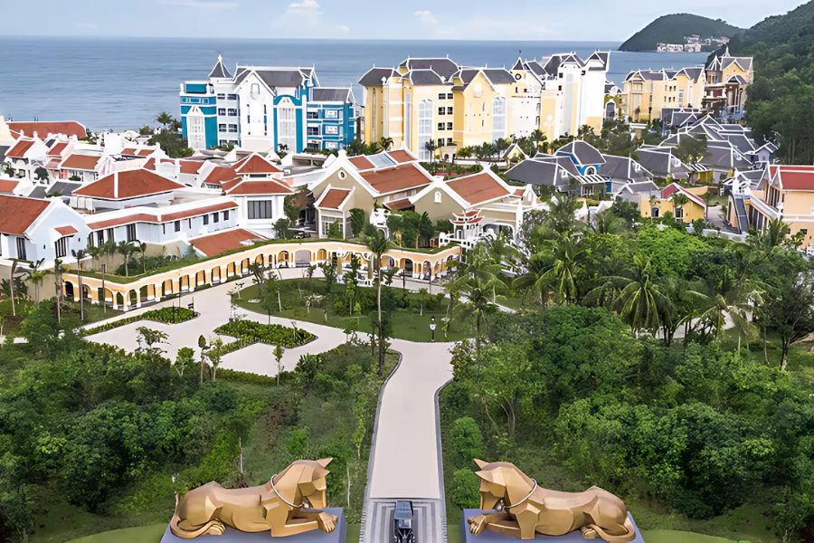 Vibrant beach resort in Vietnam with colorful buildings, lush greenery, and golden horse statues, overlooking the ocean and a scenic hillside.