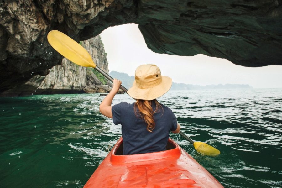 kayaking in a red kayak through a scenic sea cave with emerald waters, surrounded by rocky cliffs and distant islands, perfect for 12 days in Vietnam.