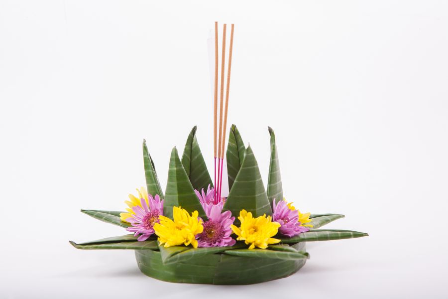 Beautifully crafted krathong made of banana leaves, vibrant flowers, a lit candle, and incense sticks, placed on a river’s edge during Loy Krathong festival in Thailand