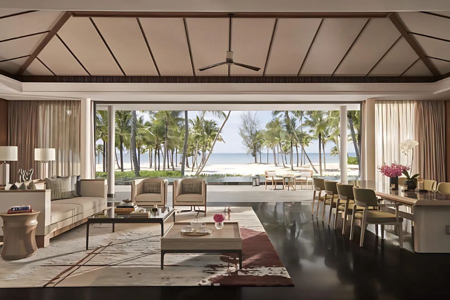 Luxurious beachfront villa interior at Regent Phu Quoc Resort in Vietnam, featuring an open living and dining area with a stunning view of the ocean and palm trees through large windows.