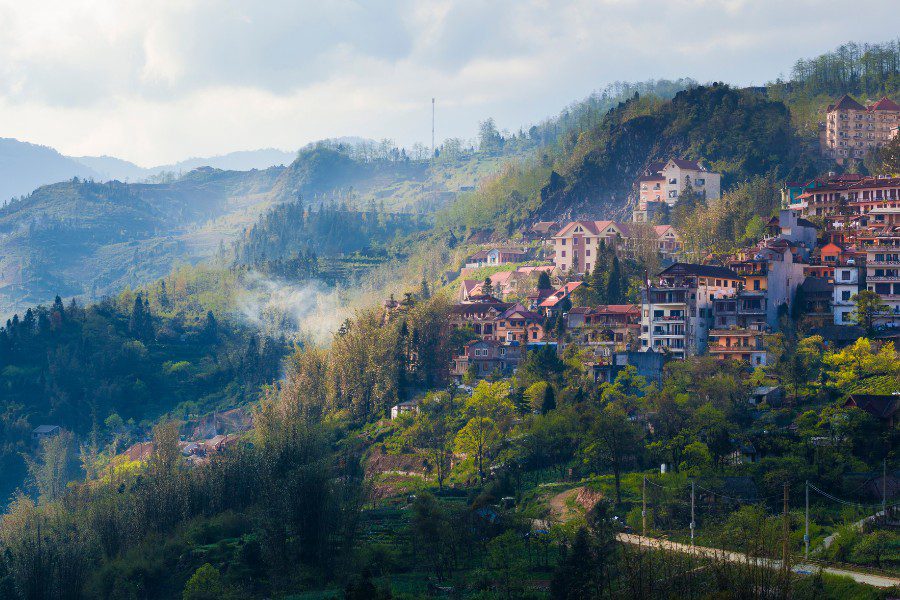 Panoramic view of a picturesque mountainside town with colorful houses nestled among lush green mountains under a cloudy sky, showcasing a serene and scenic rural landscape.