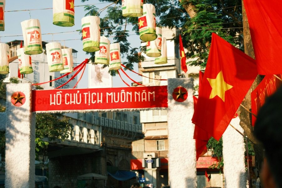 Decorative archway with Vietnamese flags and lanterns, displaying 'Ho Chi Minh Muon Nam' (Long Live Ho Chi Minh), set against a vibrant urban street, celebrating national pride.